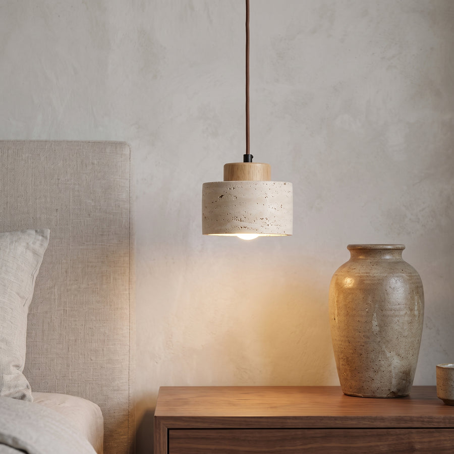 Travertine drum pendant with oak cap hanging over a bedside table