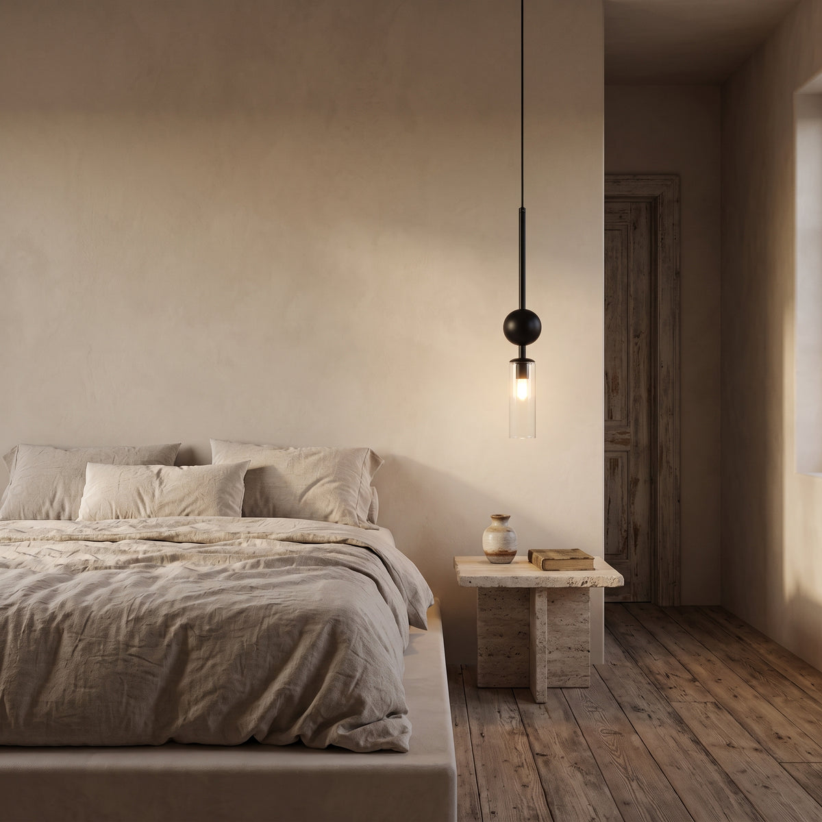 Black pendant light with clear glass tube glowing over a travertine side table