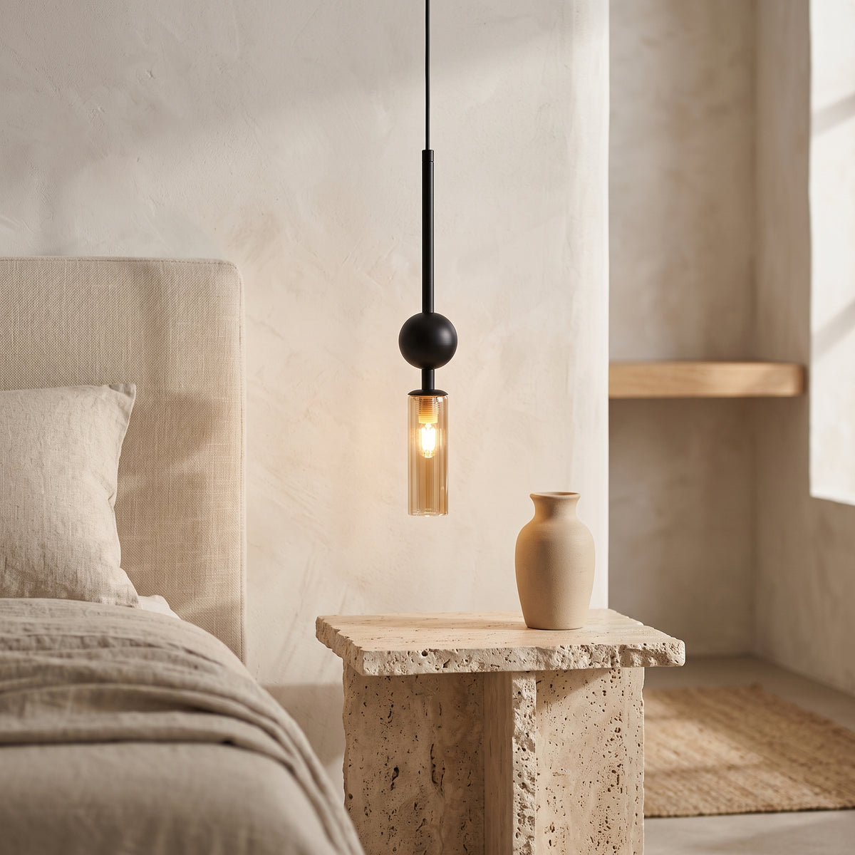 Black pendant light with an amber glass tube beside a bed