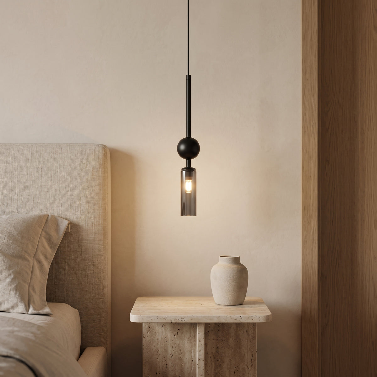 Black pendant light with a smoky grey glass tube beside a bed