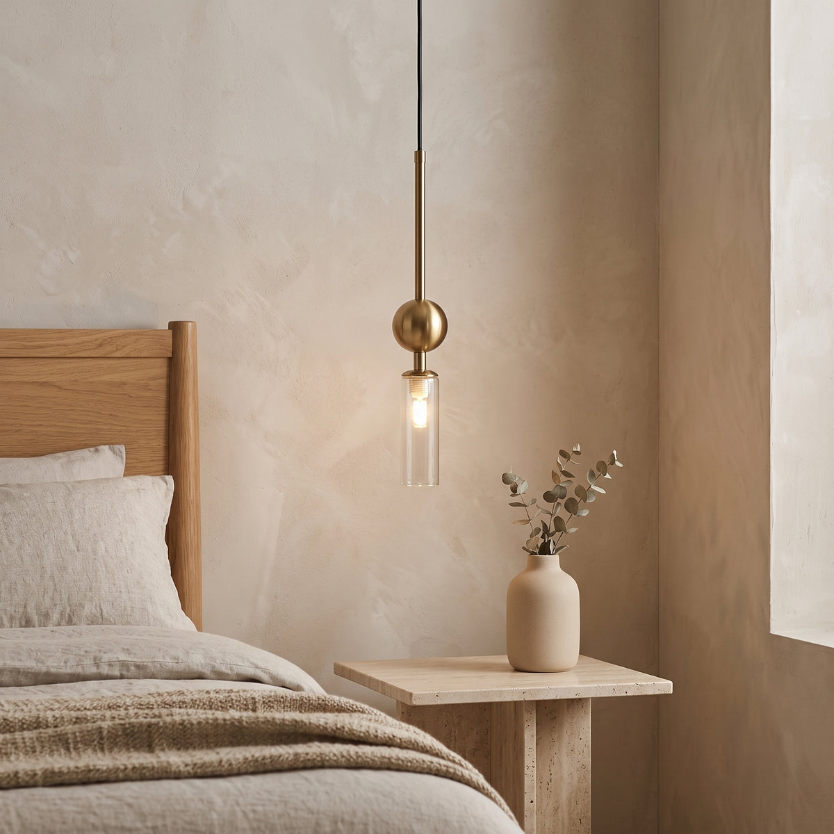 Gold pendant light with a clear glass tube beside a bed