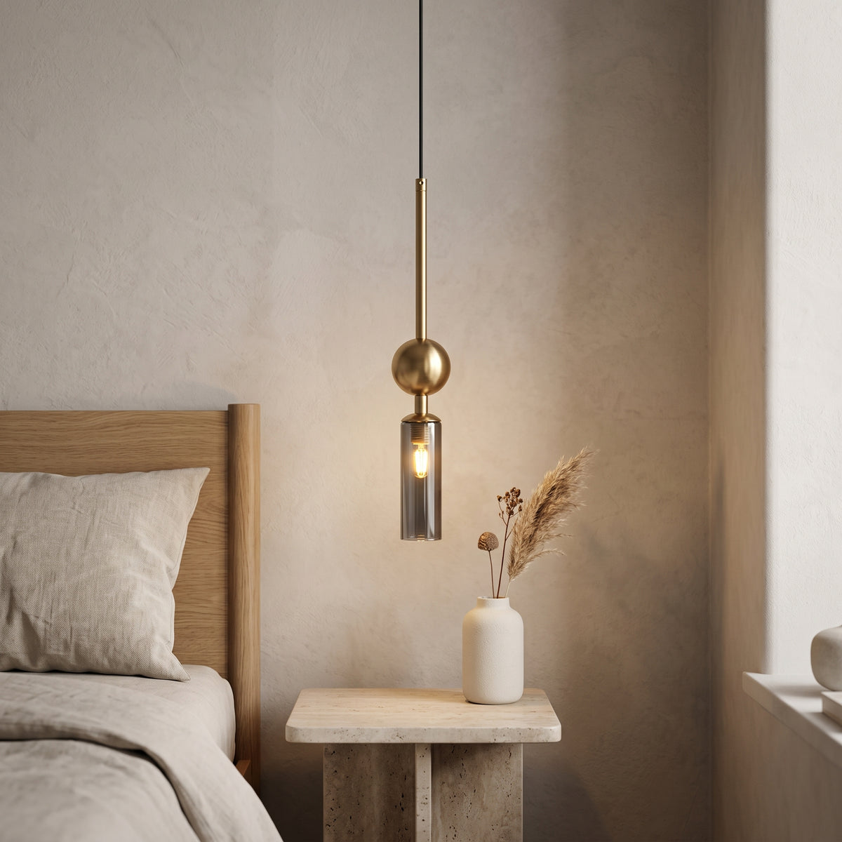 Gold pendant light with a smoky grey glass tube beside a bed