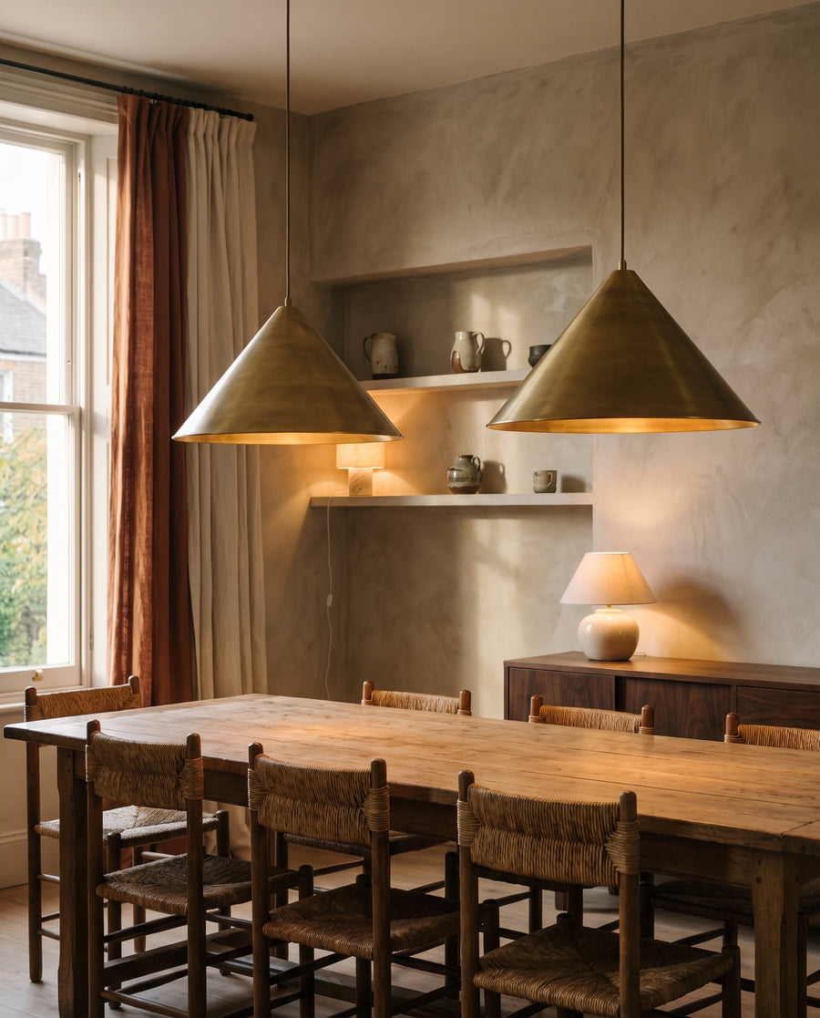 Two brass cone pendant lights glowing above a long oak dining table