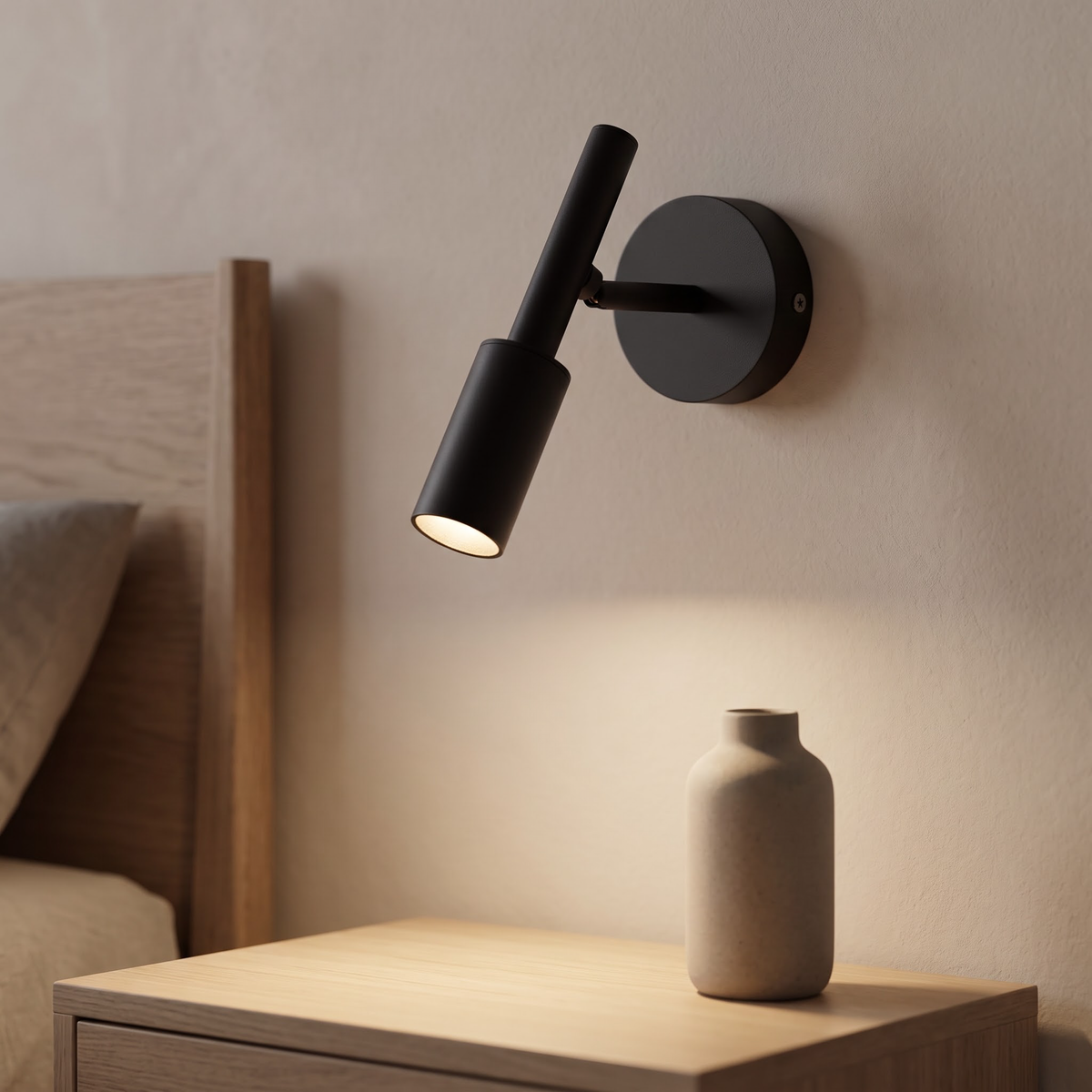 Matte black adjustable wall spot glowing above an oak nightstand