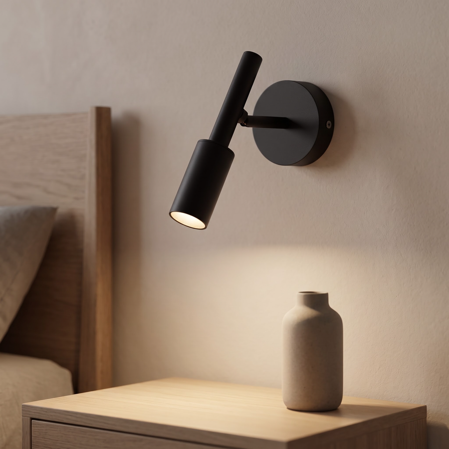 Matte black adjustable wall spot glowing above an oak nightstand