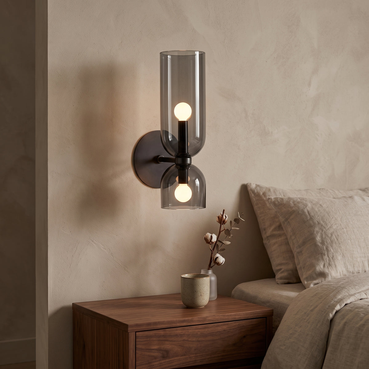 Smoky black glass wall sconce lit beside a walnut nightstand