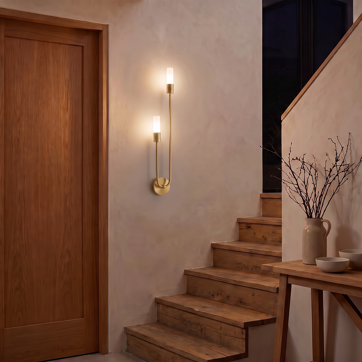Brass twin-tube wall sconce on a limewashed stairwell wall