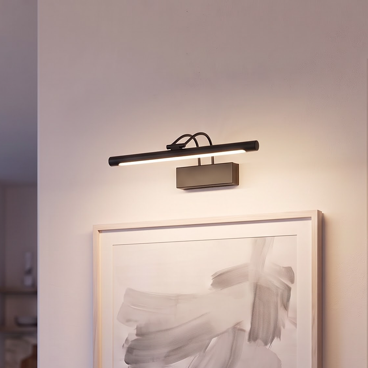 Matte black picture light glowing above an ash-framed abstract painting