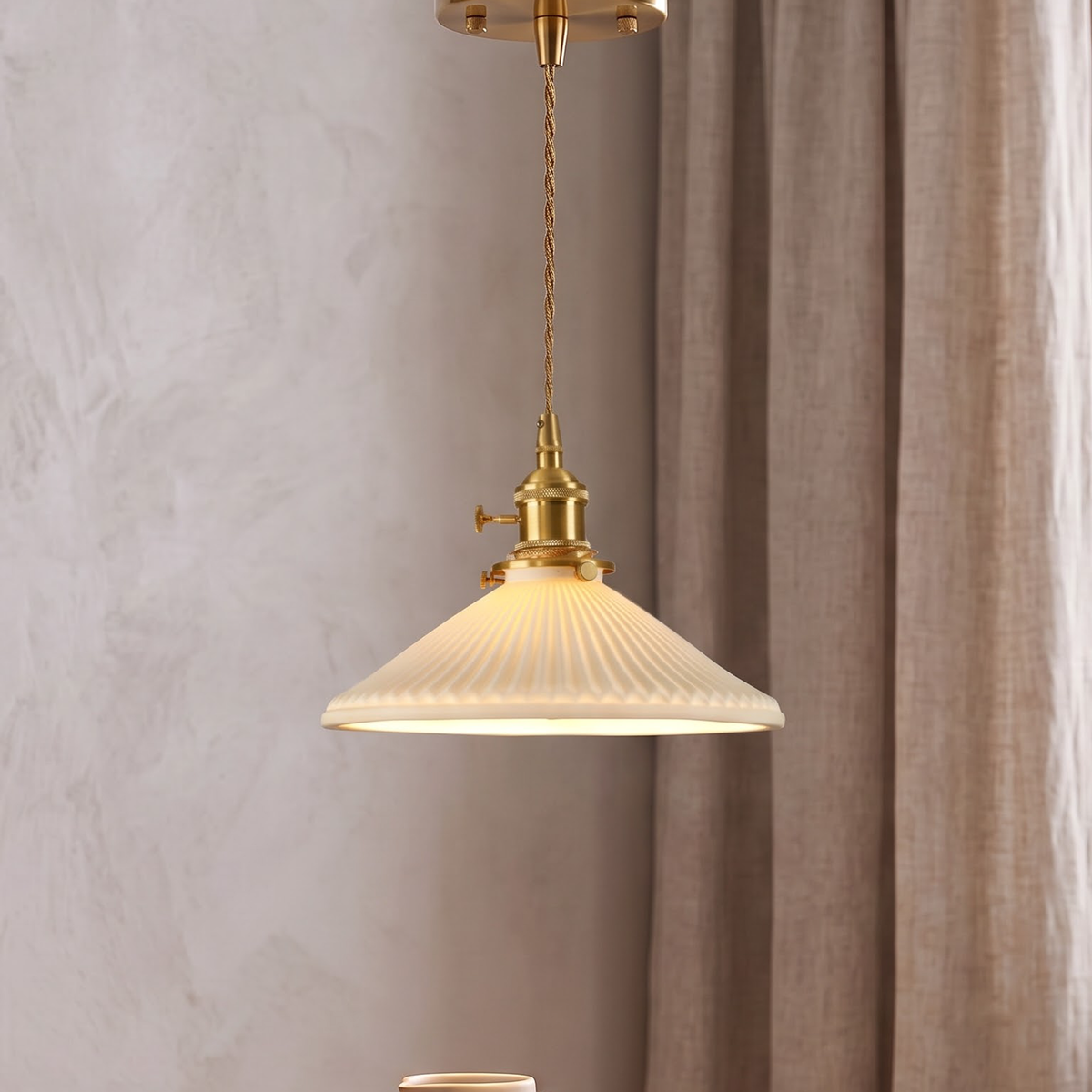 Pleated white ceramic pendant with brass socket glowing over an oak table