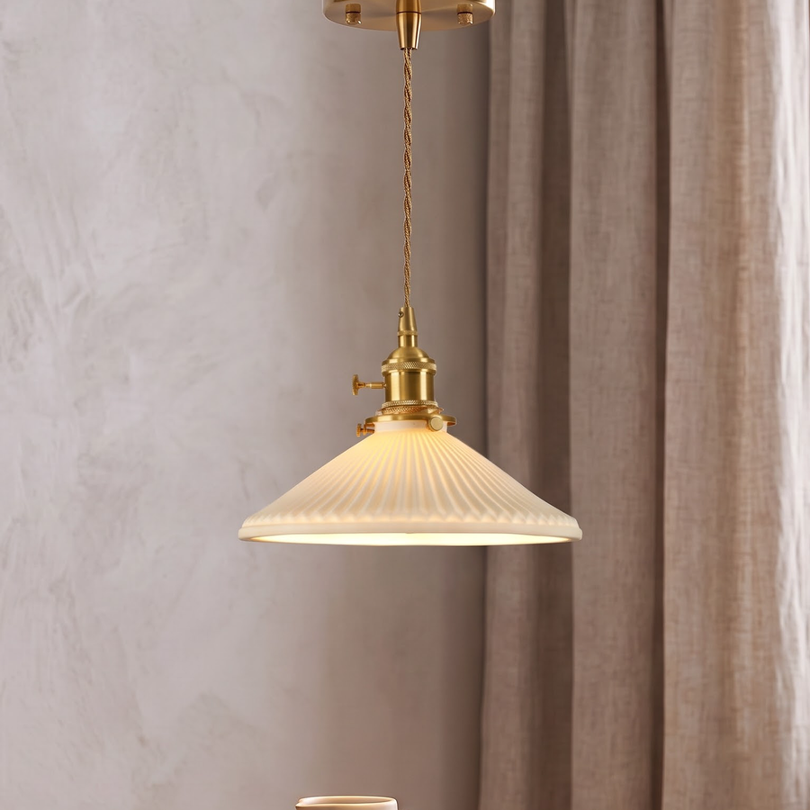 Pleated white ceramic pendant with brass socket glowing over an oak table