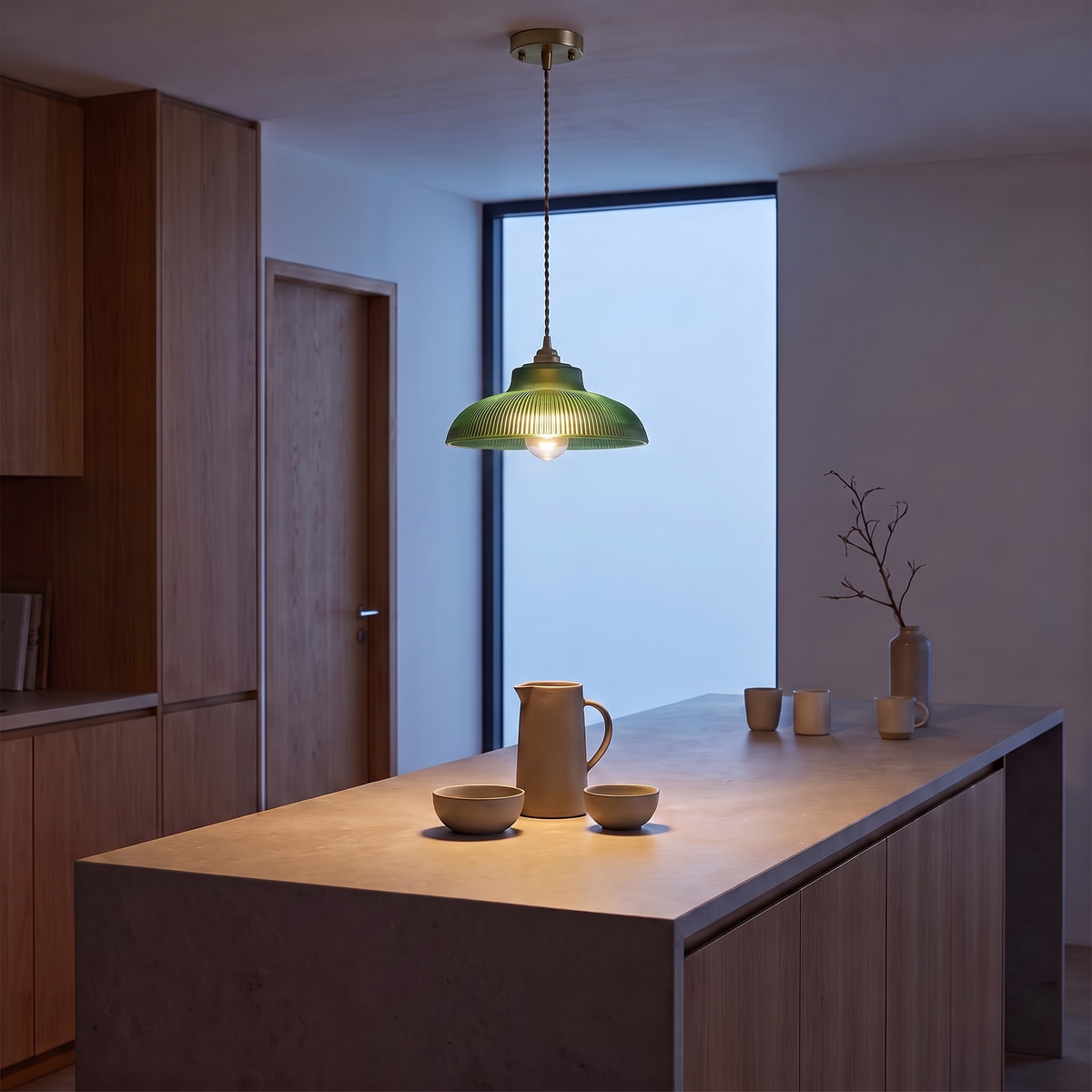 Green glass pendant light above a stone kitchen island at blue hour