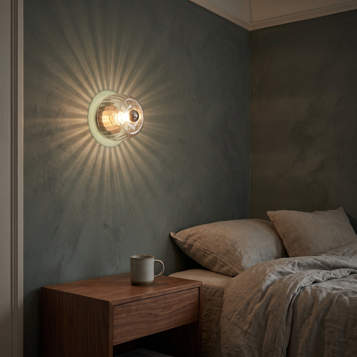 Clear ribbed glass sconce glowing over a walnut nightstand at night