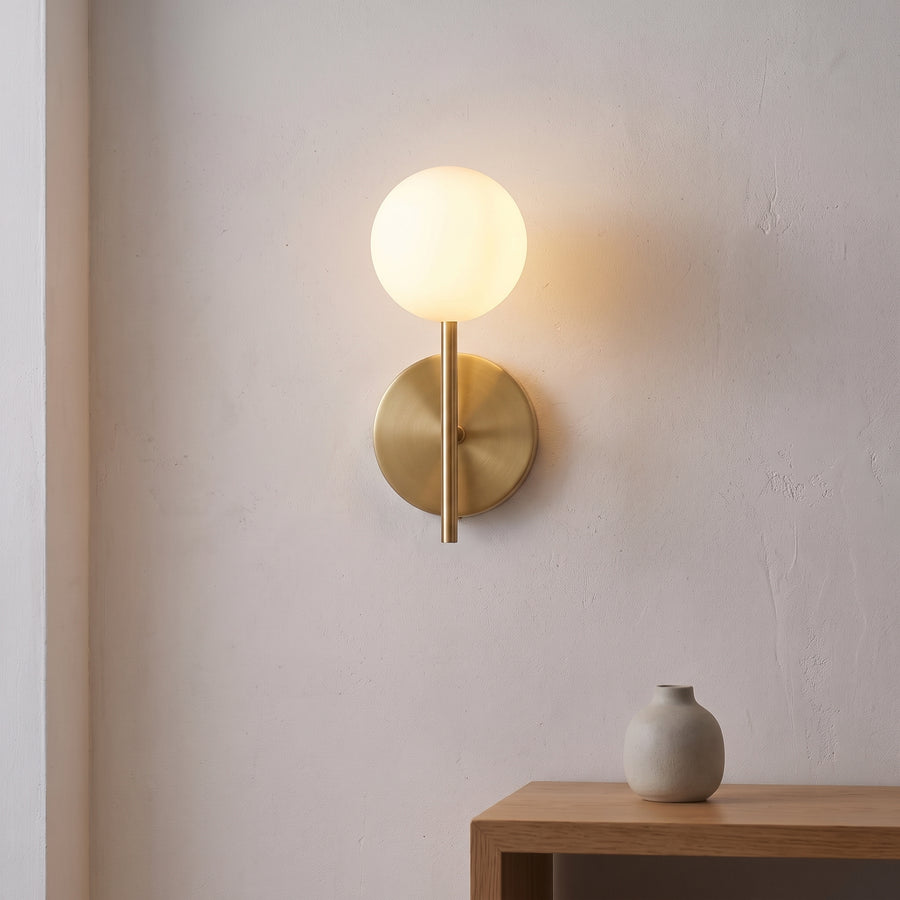 Hoshi gold wall sconce with one glowing opal globe above an oak side table
