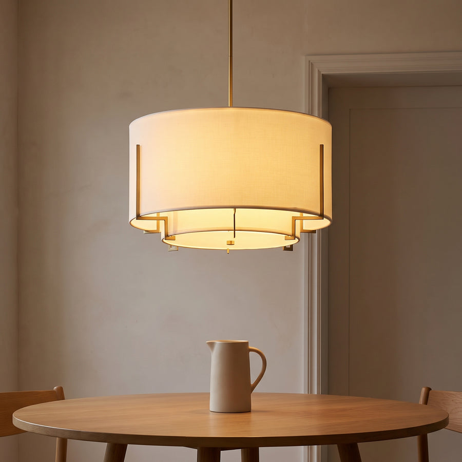 Off-white fabric drum pendant with brass frame over a round dining table
