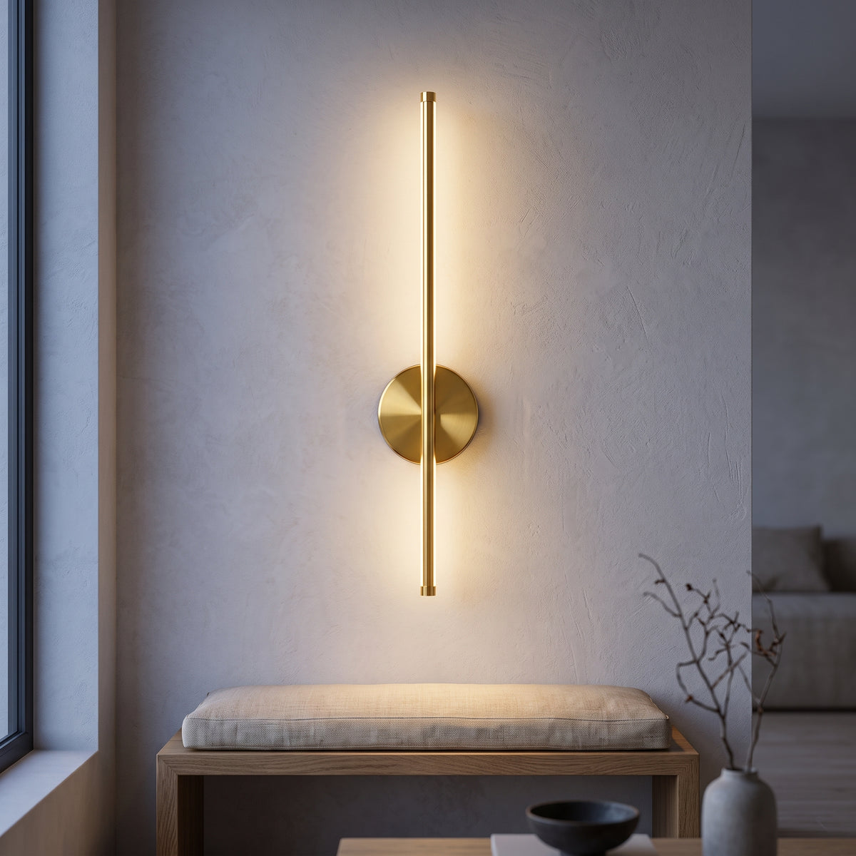 Gold rod wall sconce with round disc glowing on plaster at dusk
