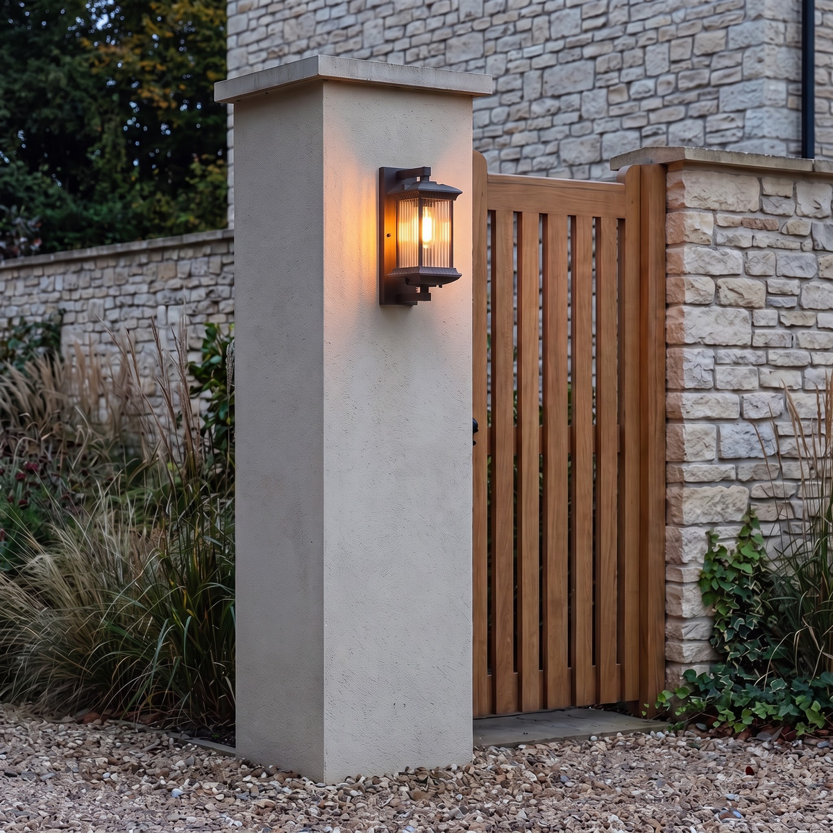 Outdoor bronze wall lantern glowing on a gate pillar at dusk