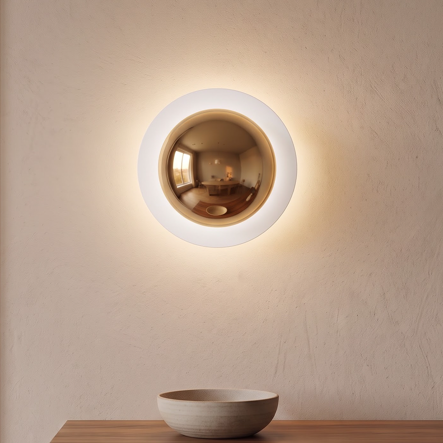 Mirror gold round wall light glowing above a walnut sideboard