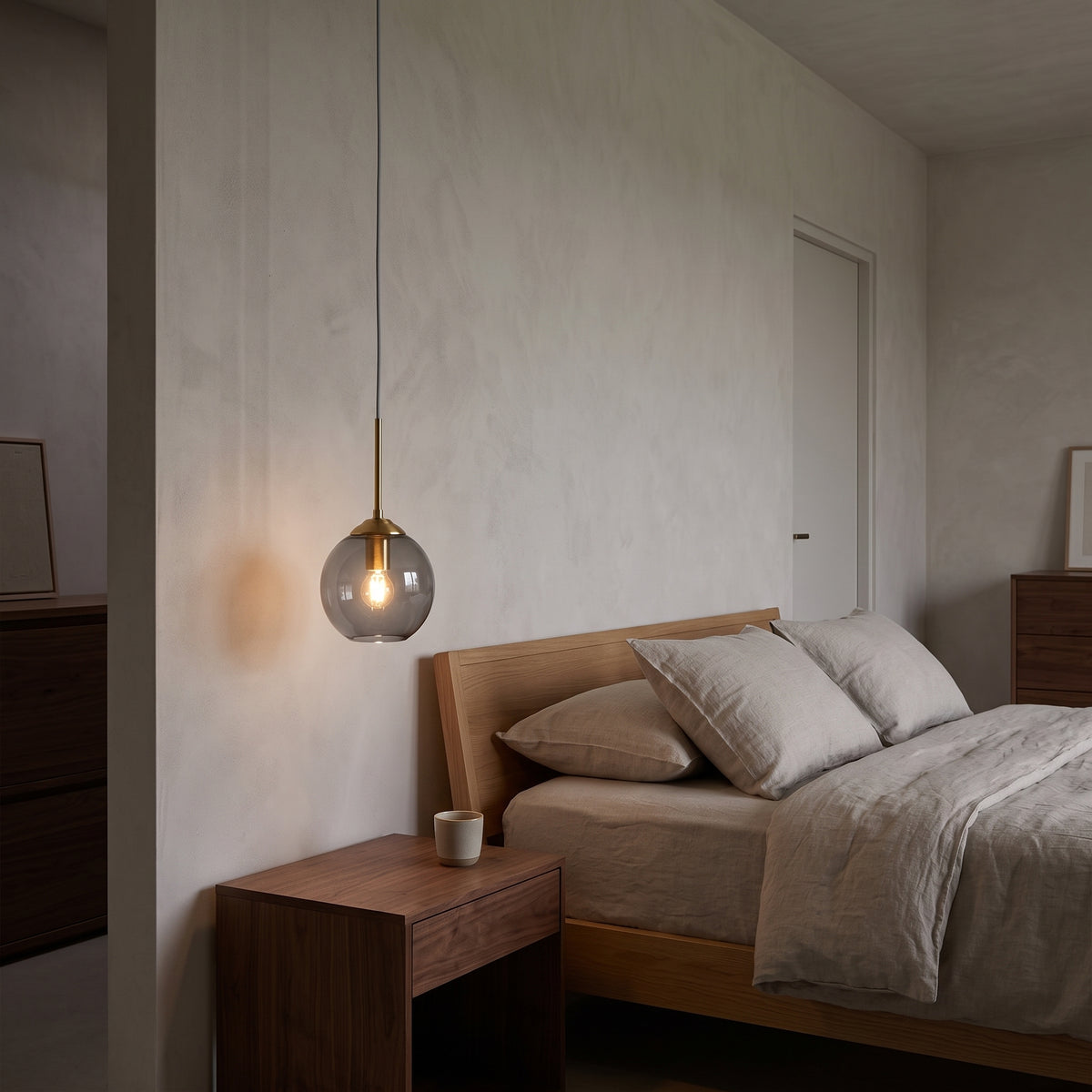 Smoky grey glass globe pendant glowing over a bedside table at dusk