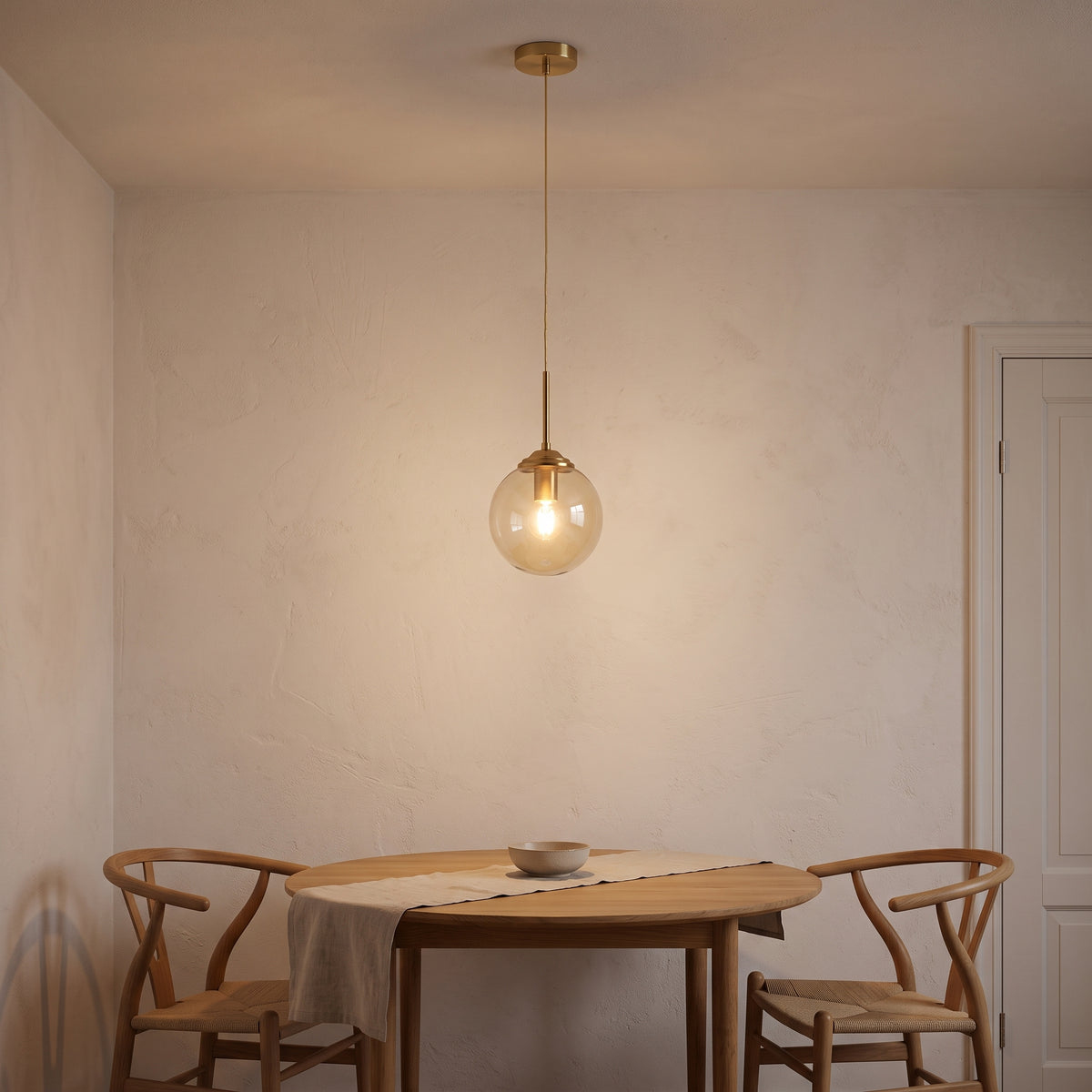 Amber glass globe pendant light over a small round oak dining table