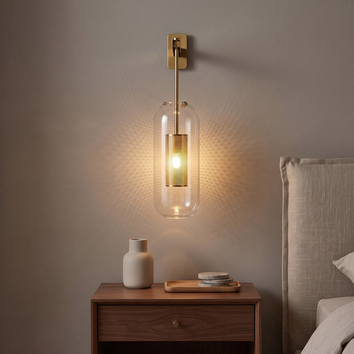 Gold and clear glass capsule wall sconce glowing above a nightstand
