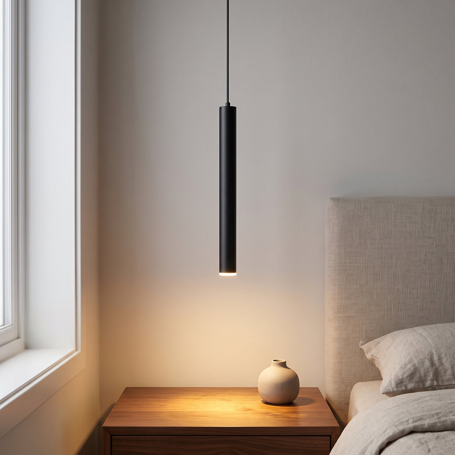 Slim black tube pendant light hanging over a walnut nightstand