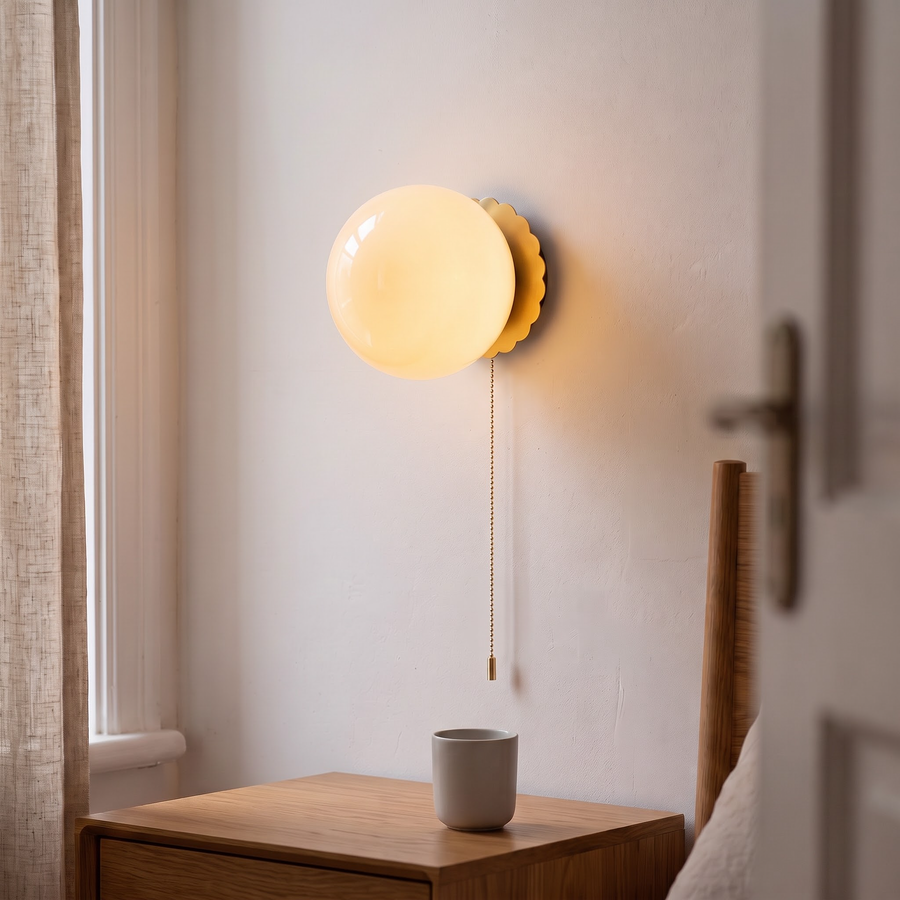Cream glass globe wall light on a gold scalloped plate with pull chain