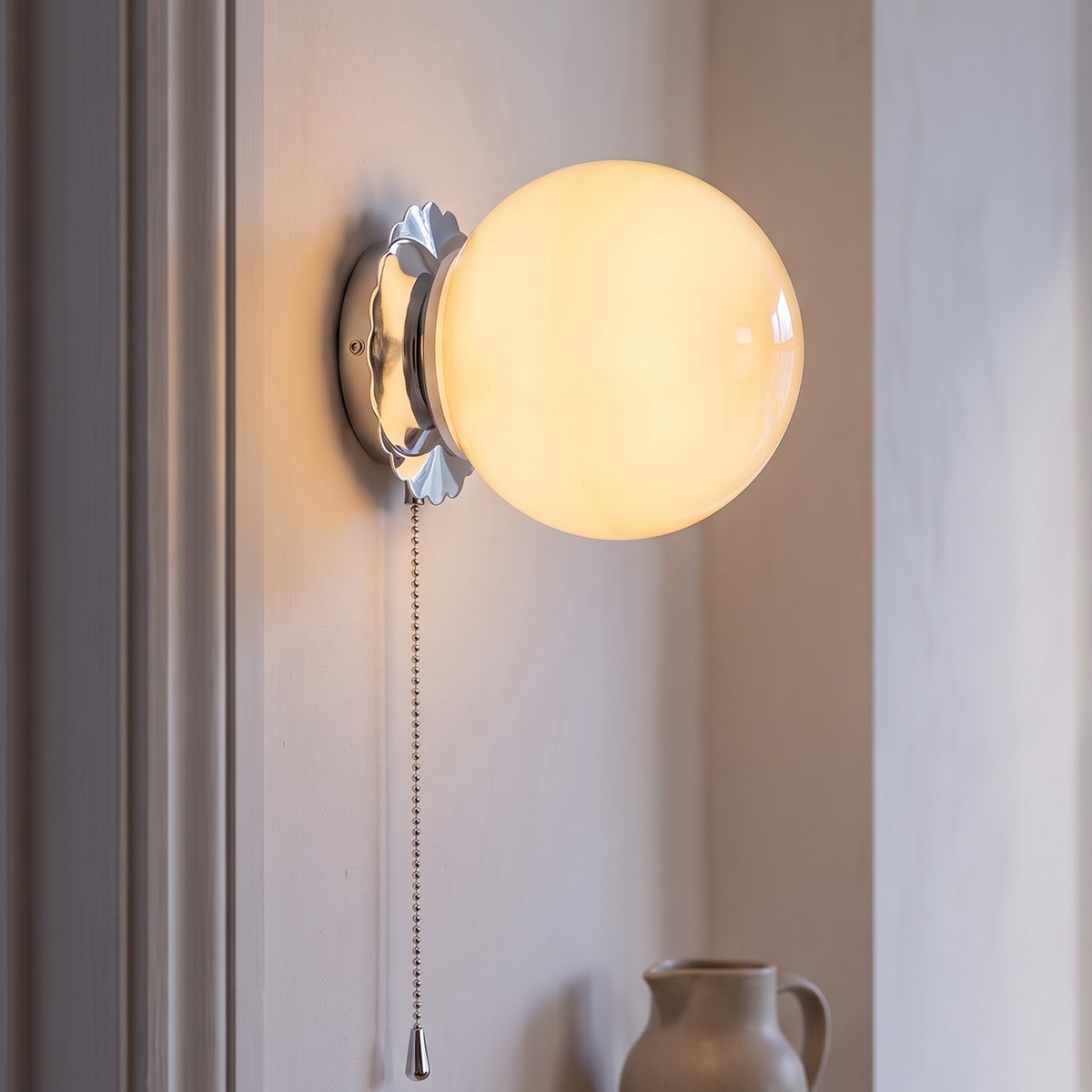Cream glass globe wall sconce on a chrome plate in a hallway