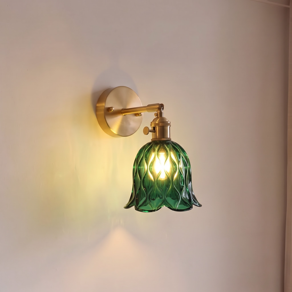 Emerald green glass bell sconce on a brass arm beside a door