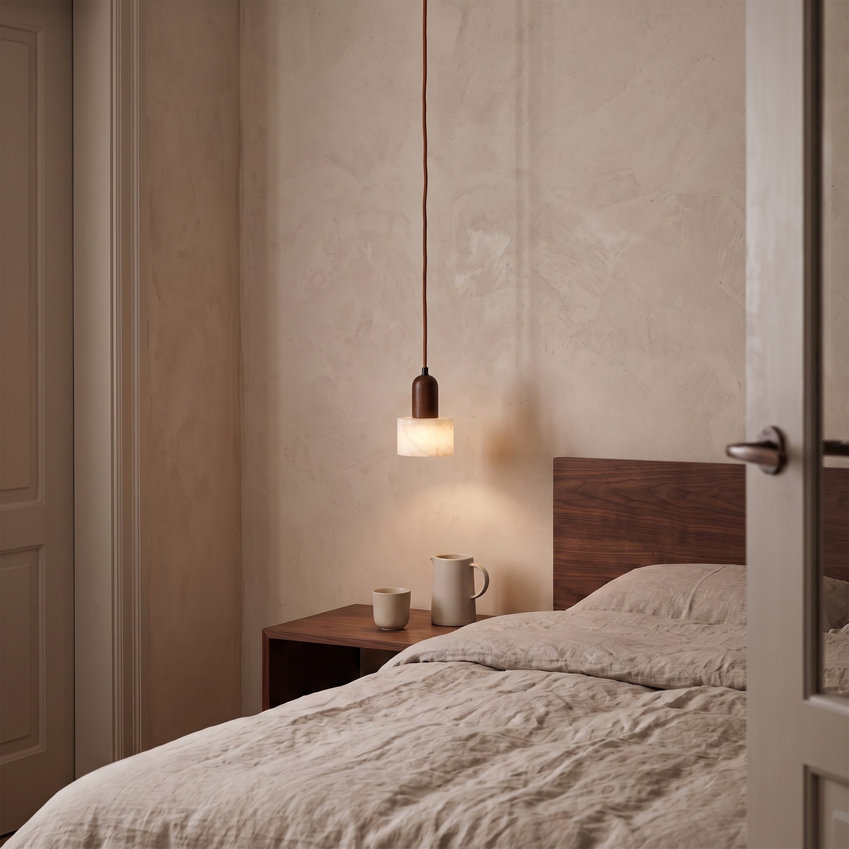 Marble bedside pendant with walnut cap glowing beside a linen bed