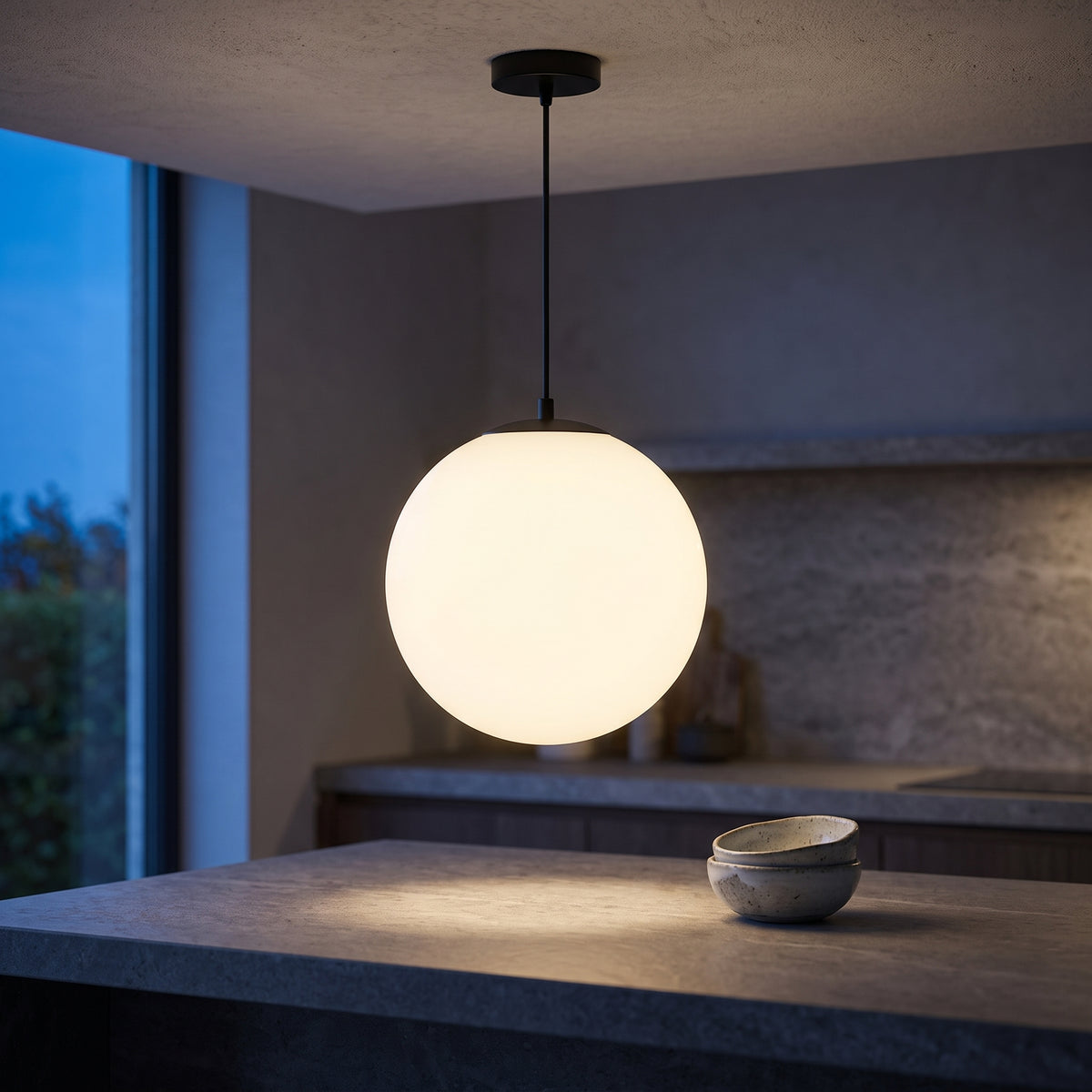 Opal globe pendant light above a stone kitchen island at blue hour