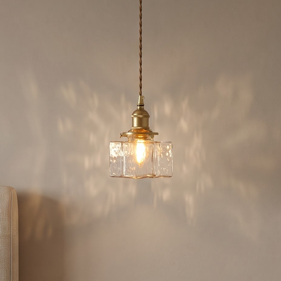Clear hammered glass cube pendant with brass socket glowing above a nightstand