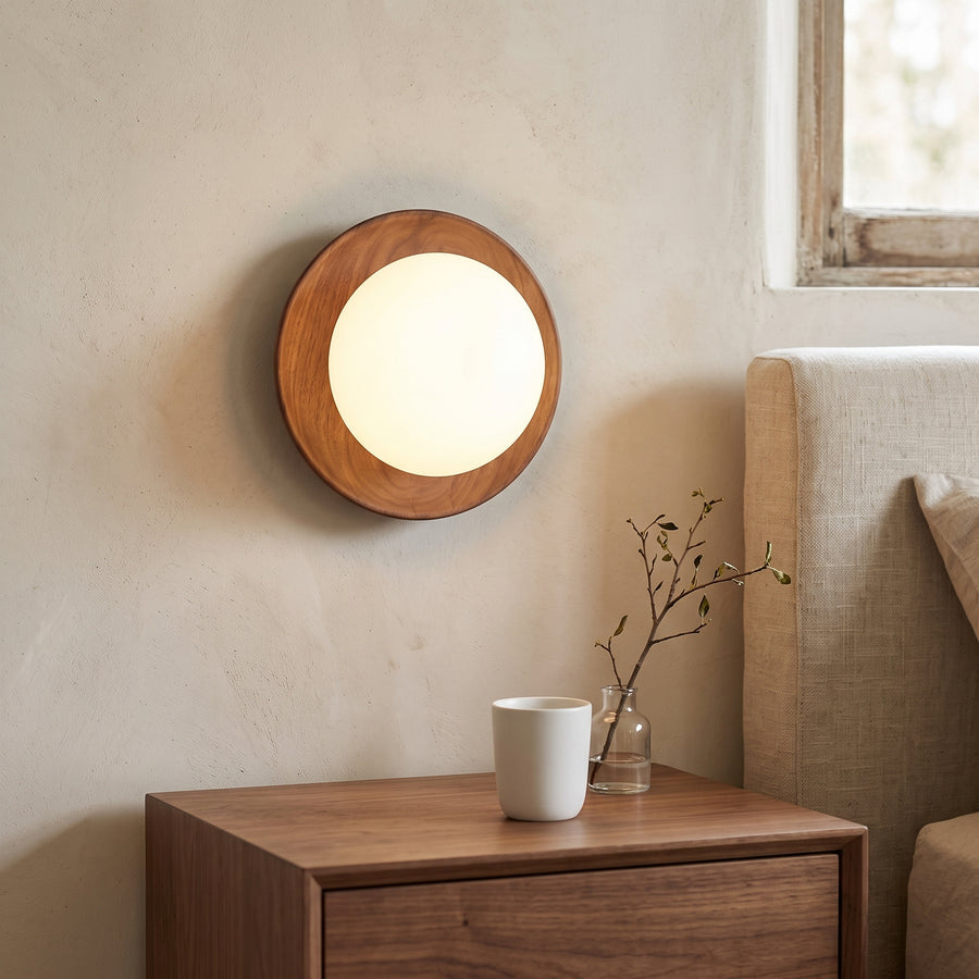 Walnut ring wall light with opal glass dome glowing beside a bed