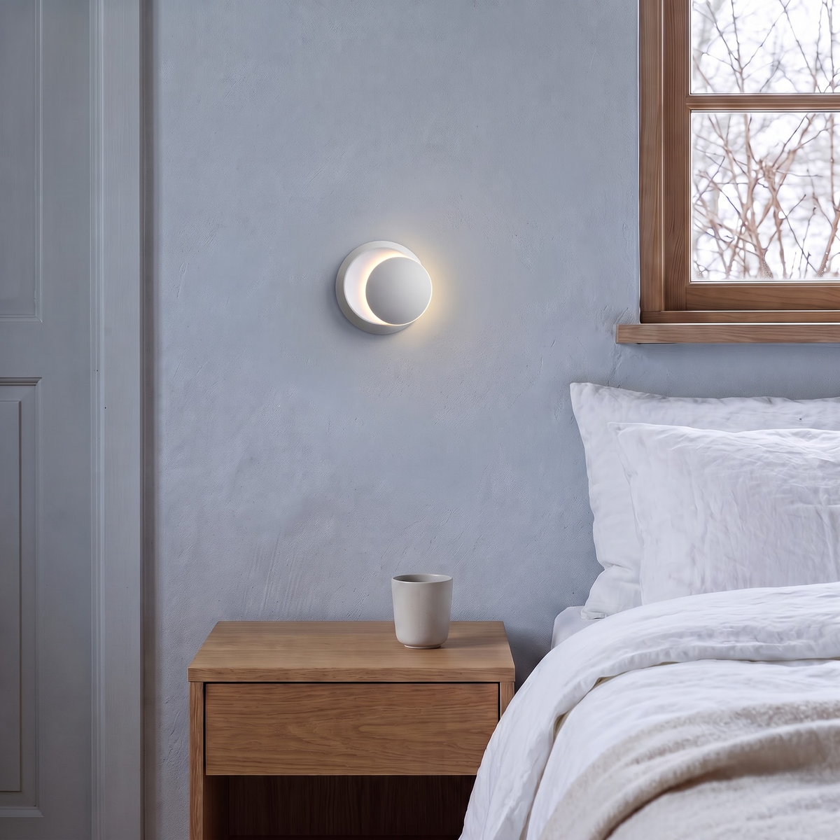 Matte white swivel disc wall light above a bedside table