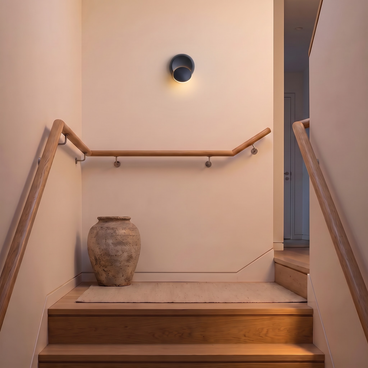 Black round swivel wall light glowing on a stair landing wall
