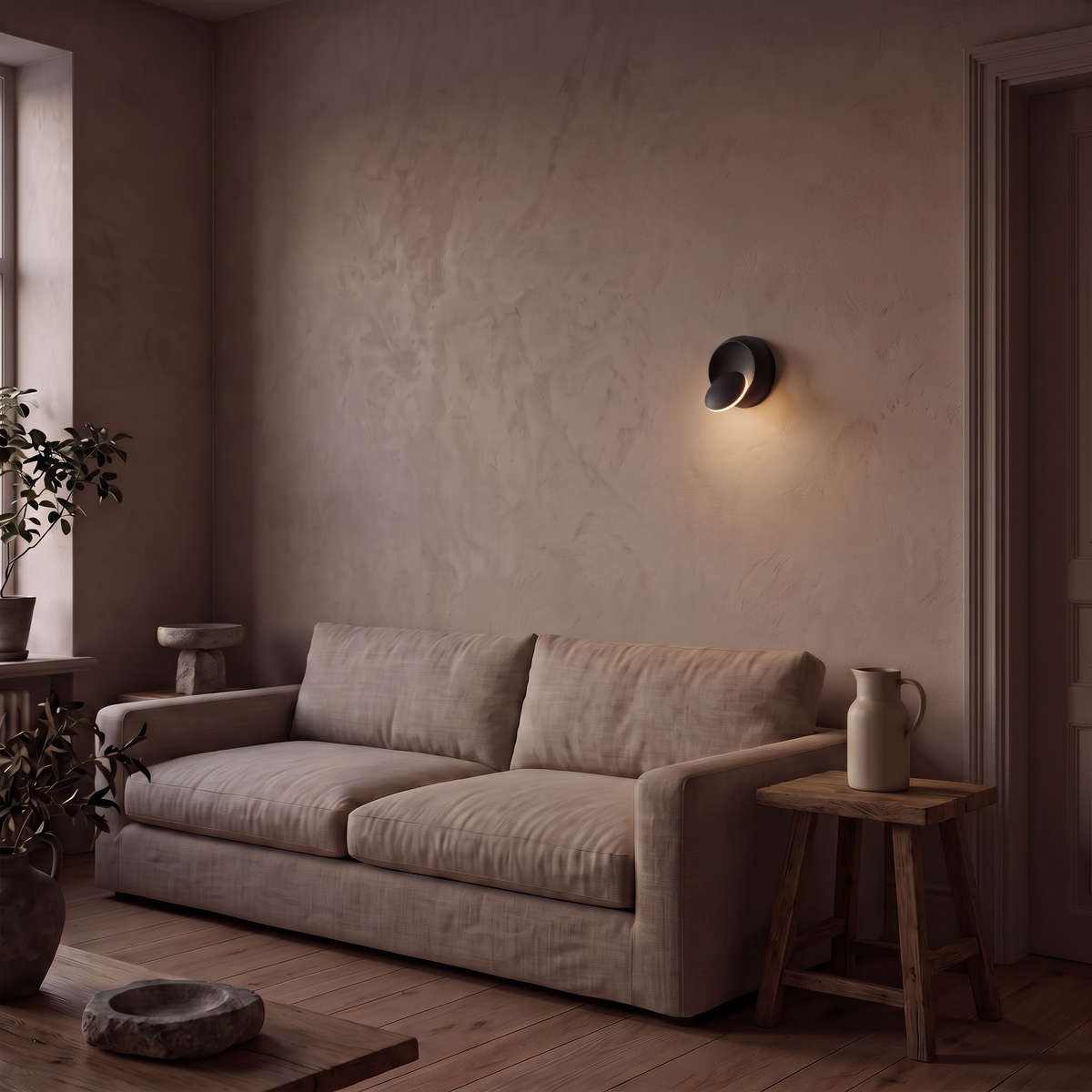 Small black disc wall sconce above a linen sofa at dusk