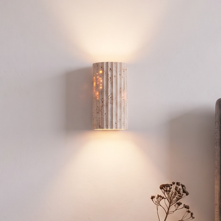 Small fluted travertine wall sconce glowing above a walnut nightstand