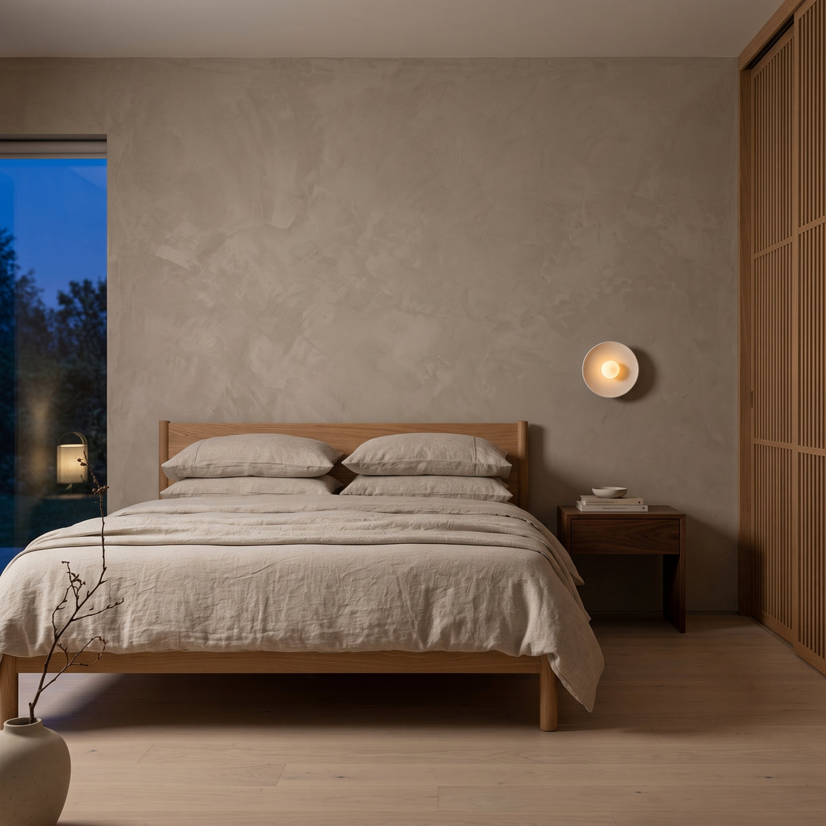 White ribbed disc wall sconce beside a linen bed at dusk