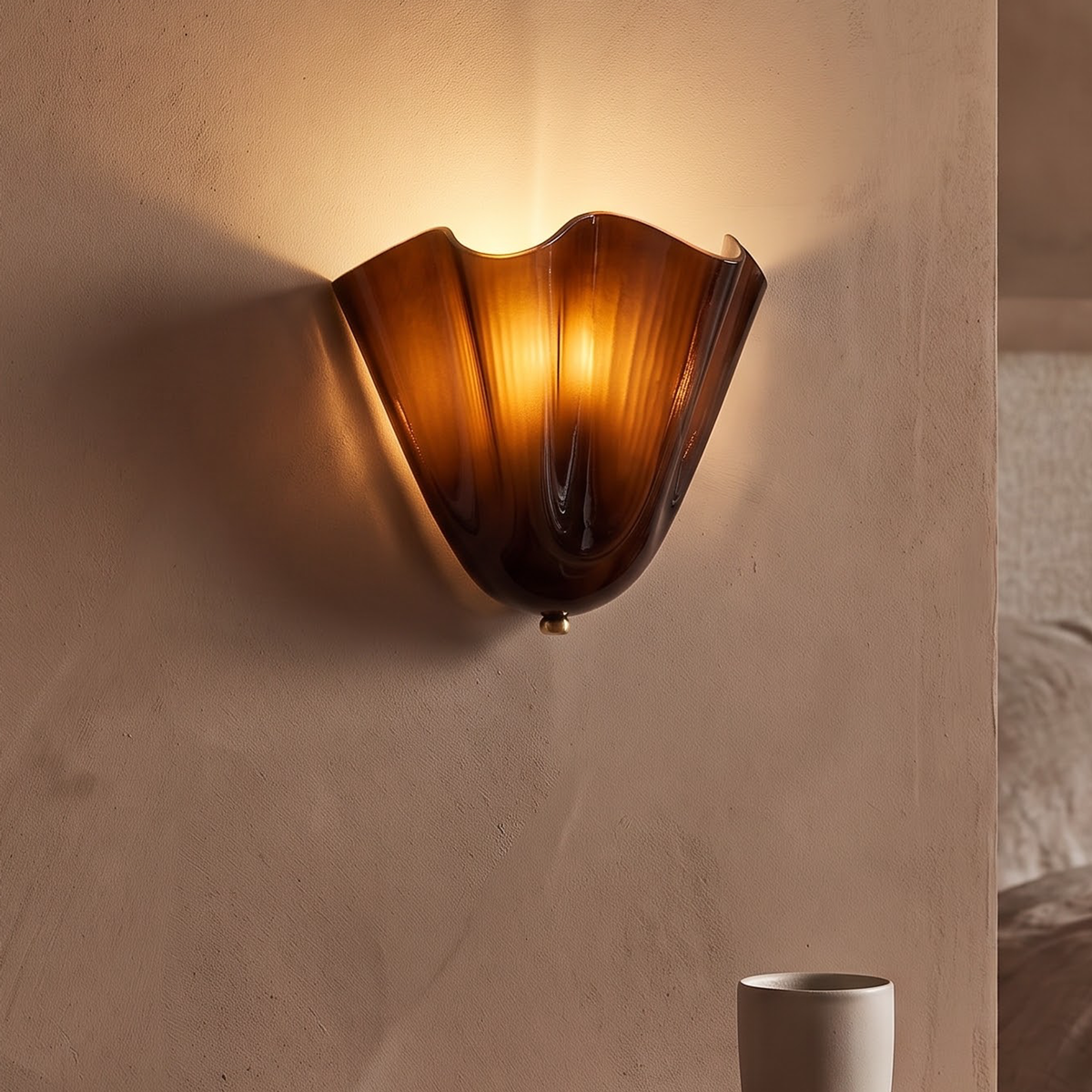 Coffee brown glass flower wall sconce glowing above a walnut nightstand