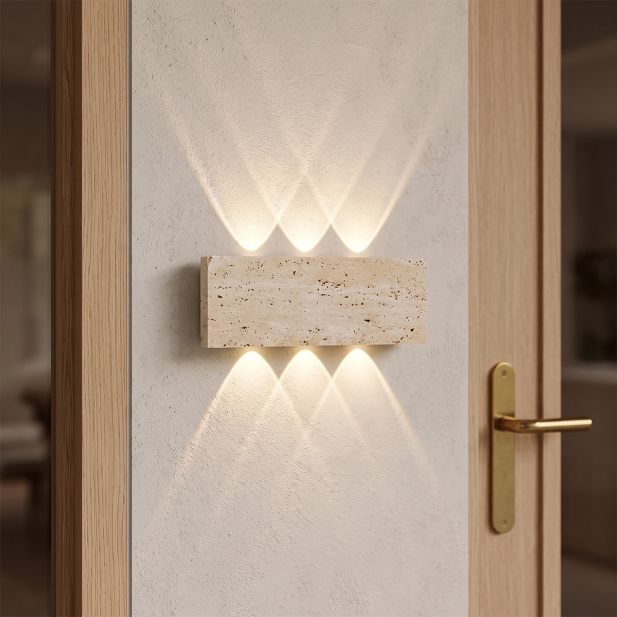 Travertine stone wall light casting fans of warm light in an entry