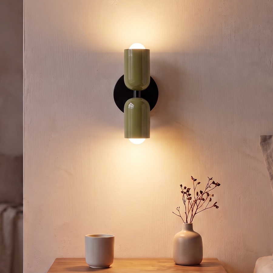Olive green up and down wall sconce glowing above a nightstand