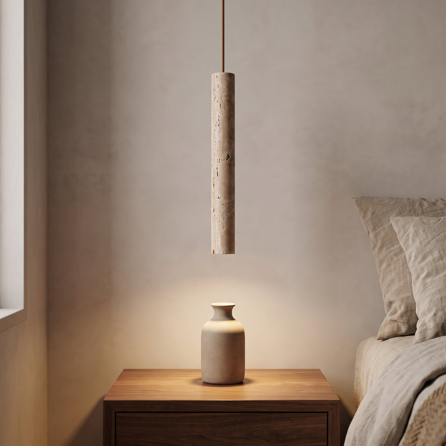 Slim travertine tube pendant above a walnut nightstand in warm evening light