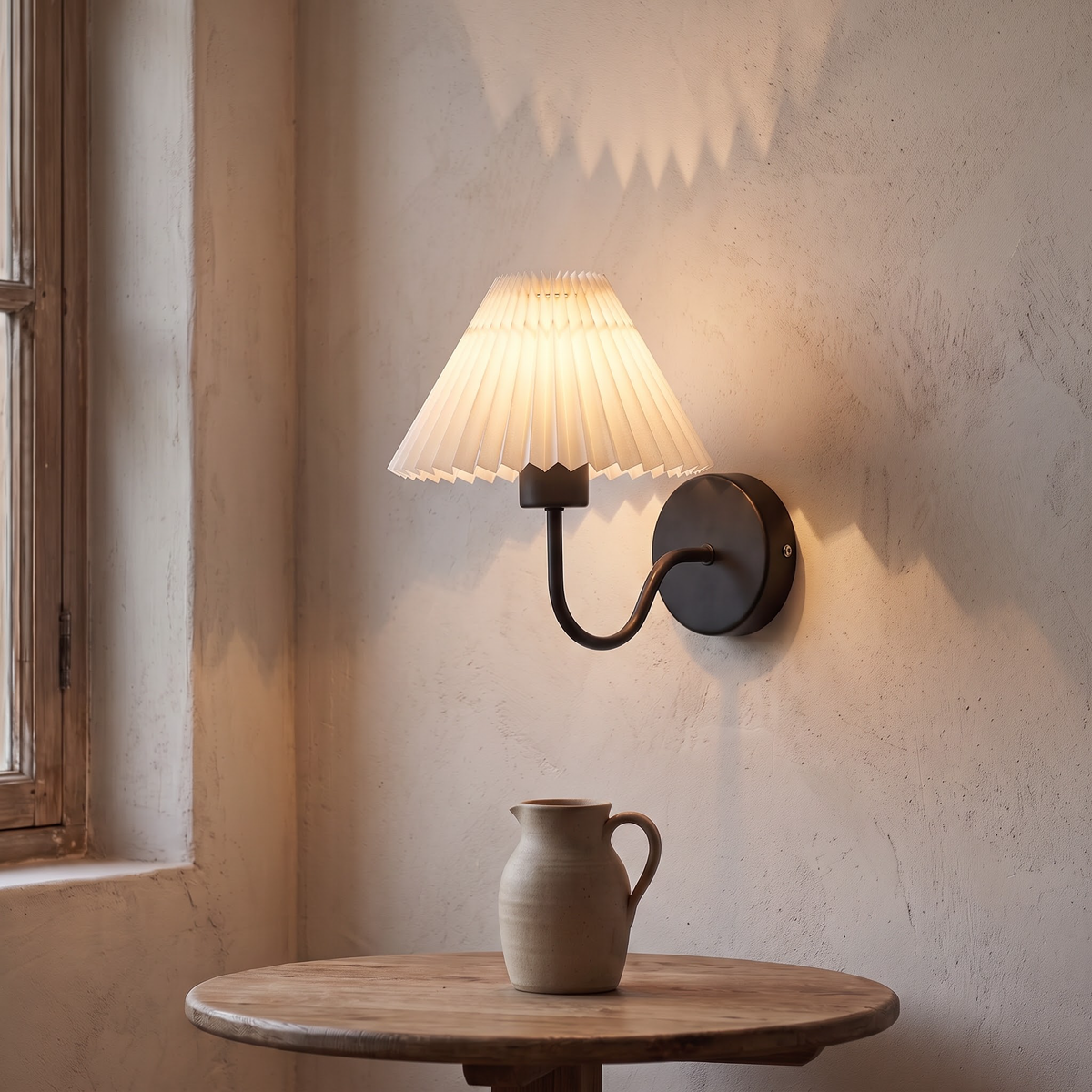 Black pleated shade wall sconce glowing above a small oak table
