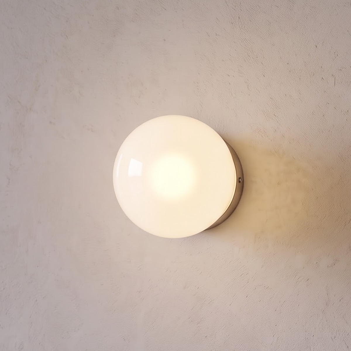 Glossy opal glass globe wall sconce glowing beside an oak door