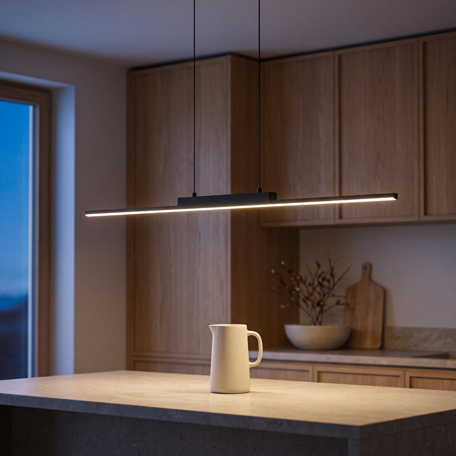 Slim black linear pendant light glowing over a stone kitchen island