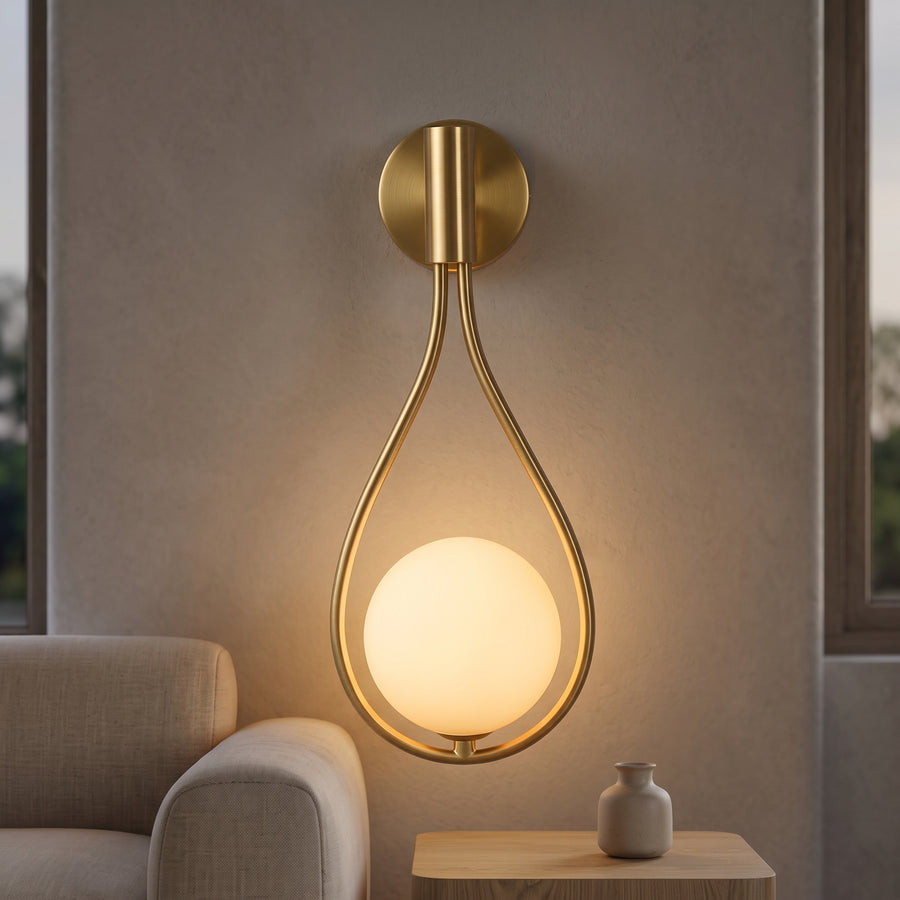 Gold teardrop wall sconce with opal globe glowing on plaster wall