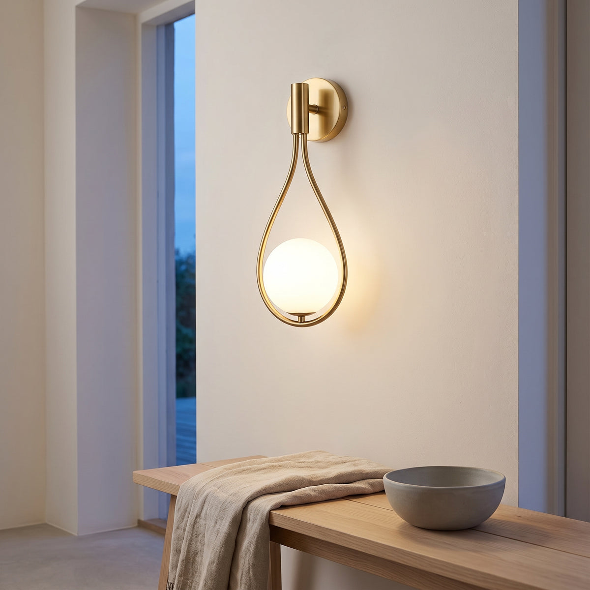 Gold teardrop wall sconce lighting a Nordic entry hallway at dusk