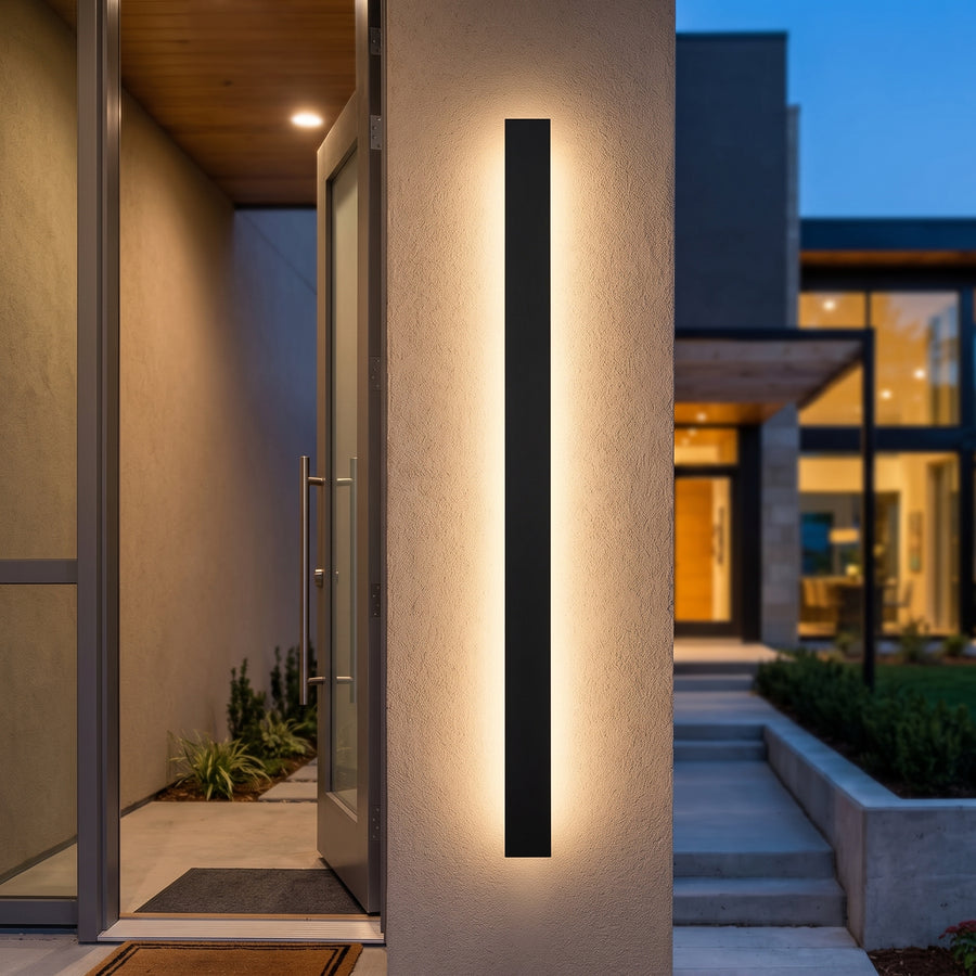 Black linear outdoor wall lamp washing a stucco entrance wall at blue hour