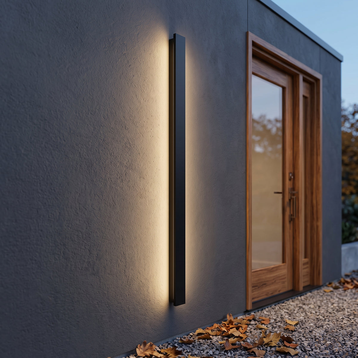 Black outdoor linear wall lamp on dark cladding beside a door at dusk