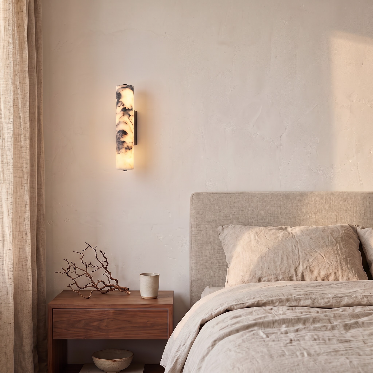 Veined stone wall sconce above a walnut nightstand beside a linen bed