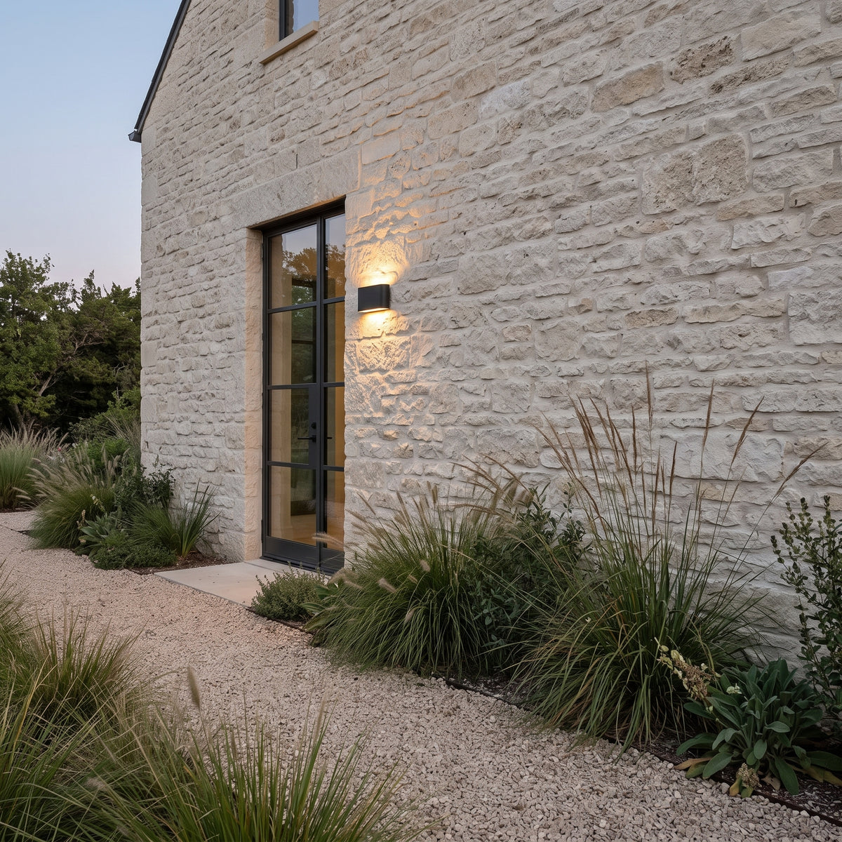 Black outdoor block wall light on a limestone wall at twilight
